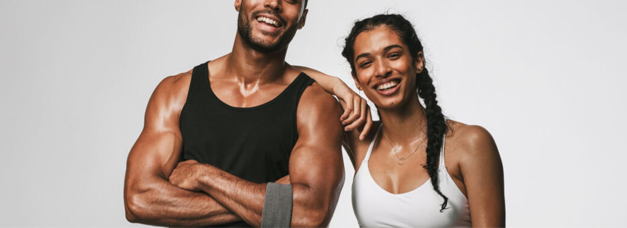 Two fit people in athletic clothing stand side by side, smiling at the camera against a plain white background.