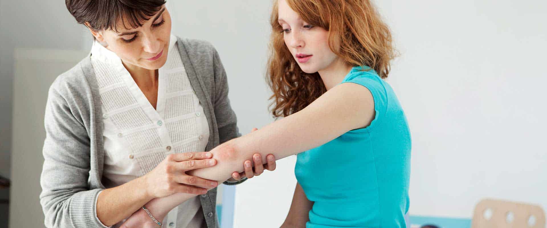 A healthcare professional examines a young woman's arm in a clinical setting.