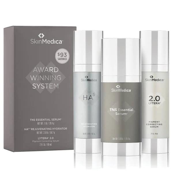 Three SkinMedica skincare products—TNS Essential Serum, HA⁵ Rejuvenating Hydrator, and Lytera 2.0—stand beside their box labeled "Award Winning System.
