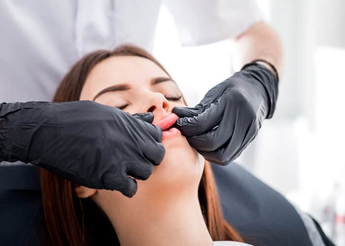 A person wearing black gloves examines a woman's upper and lower gums while she is seated in a dental chair.