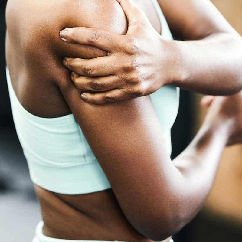 Person wearing a light blue sports bra holds their shoulder with one hand, possibly indicating discomfort or injury related to low muscle tone.