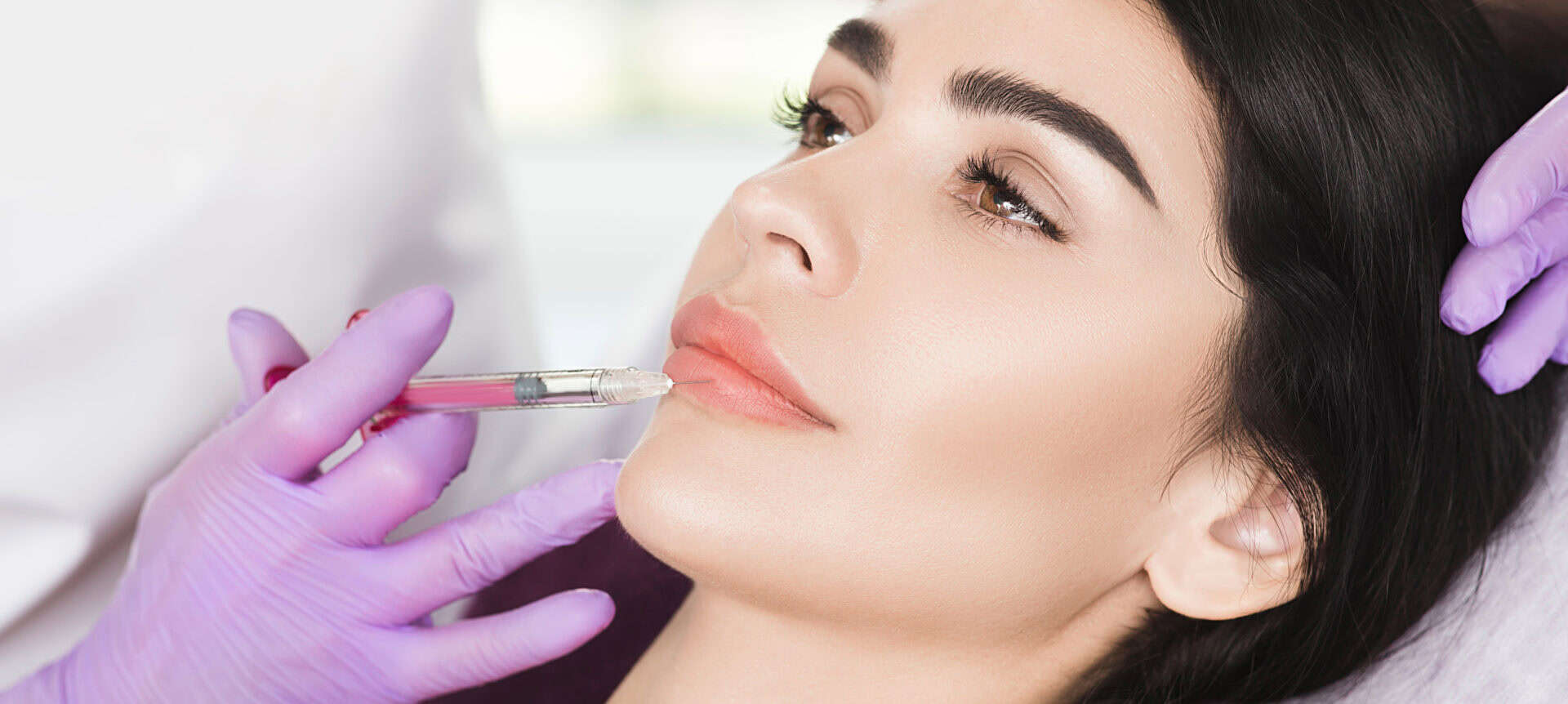 A person receives lip fillers from a local provider wearing purple gloves.